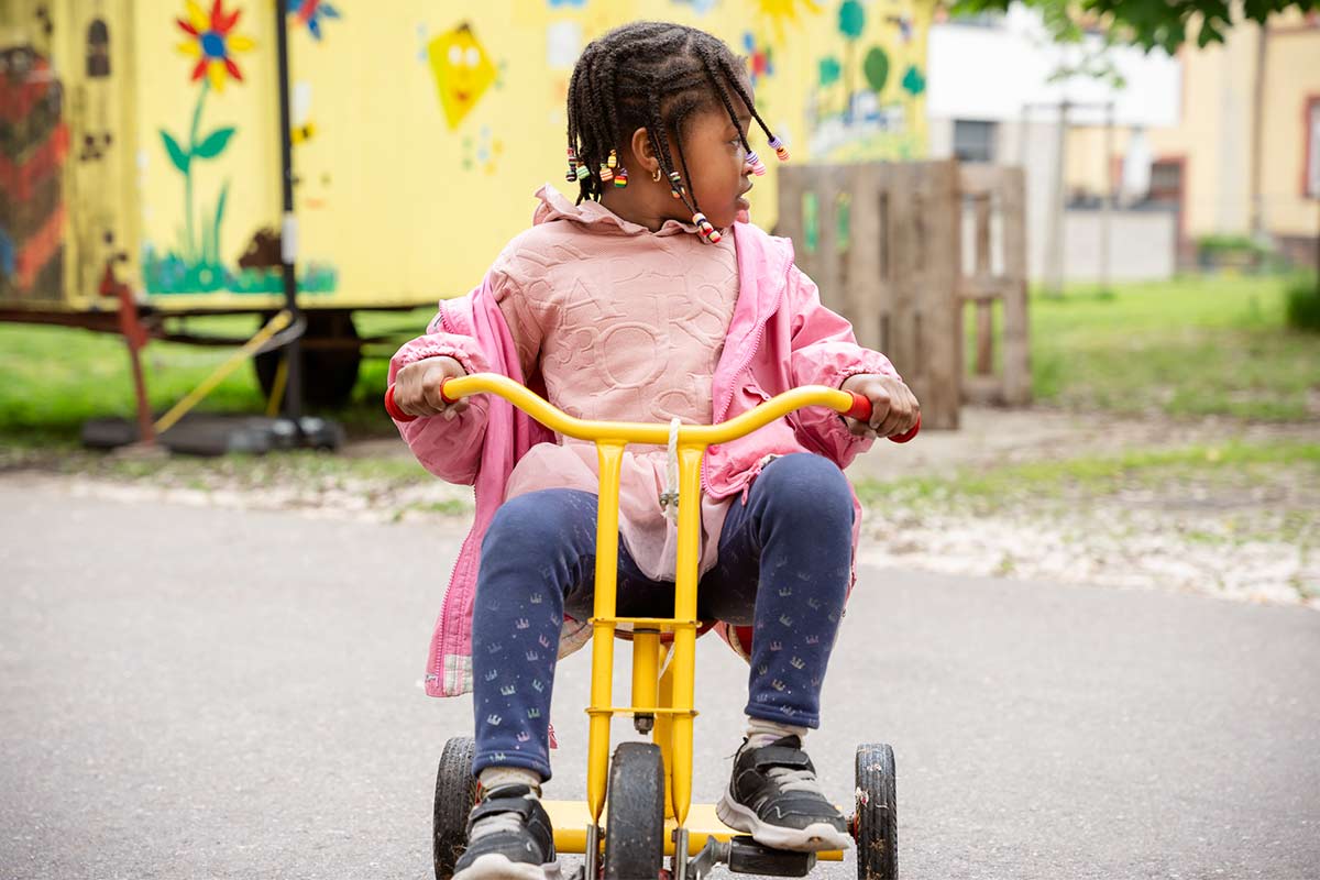 Mädchen fährt auf Dreirad im Hof, Kindertagesstätte Rasselbande