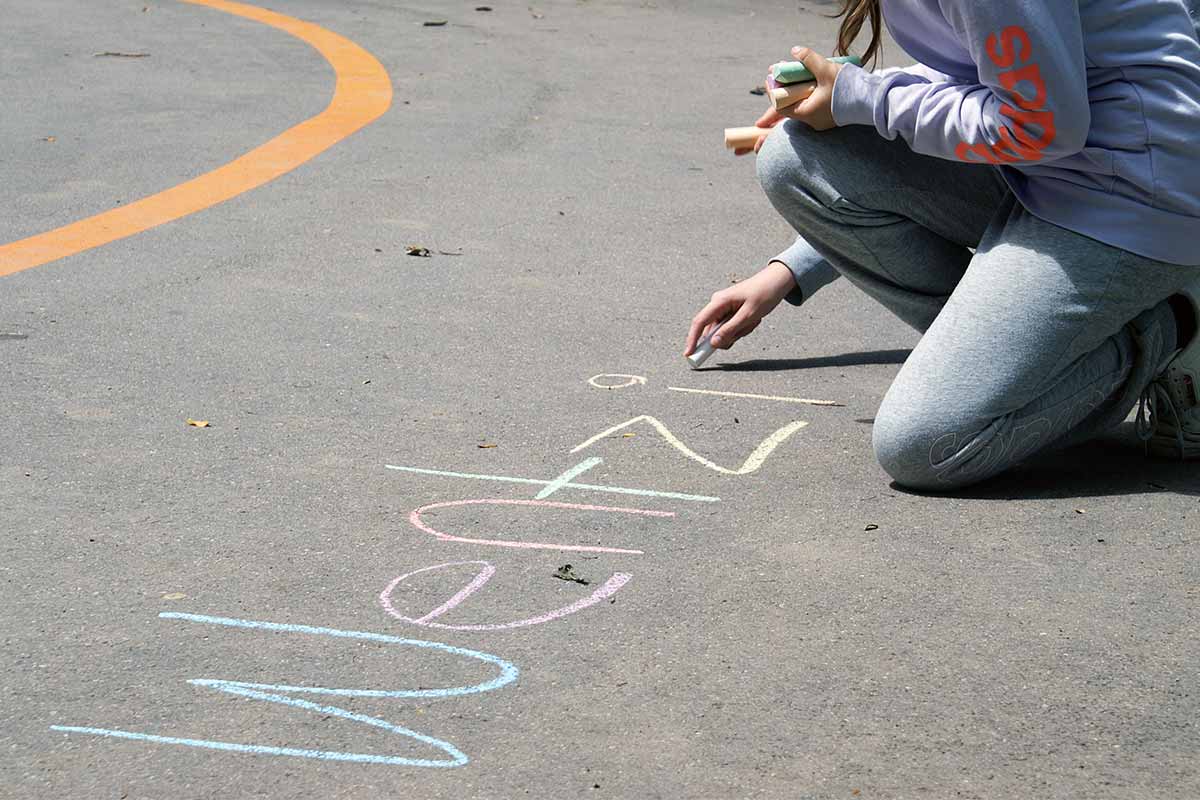 Kind schreibt mit Kreide auf den Schulhof